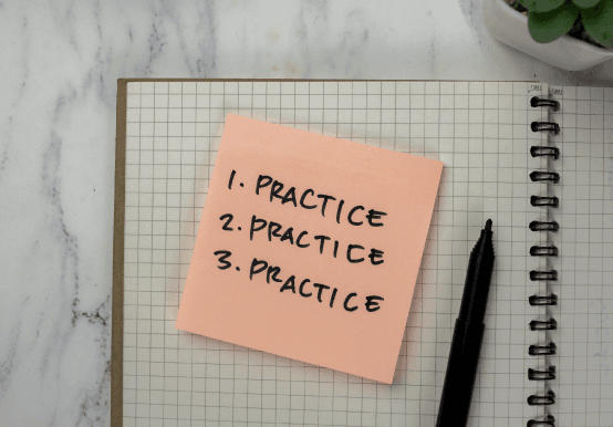 Grid lined notepad with small not saying 1. practice 2. practice 3. practice and a black pen to the right 